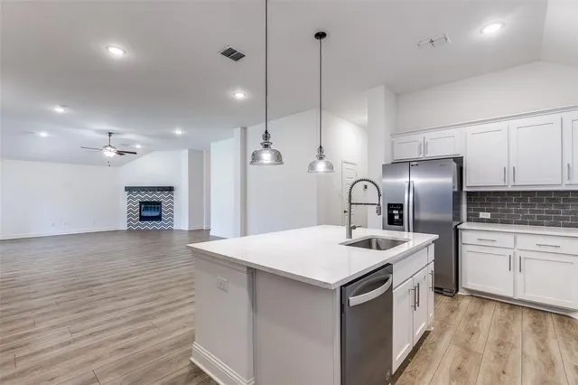 a kitchen with a sink dishwasher a refrigerator and white cabinets with wooden floor
