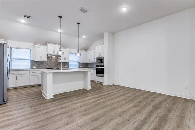 a large white kitchen with kitchen island a sink a stove a refrigerator and white cabinets with wooden floor