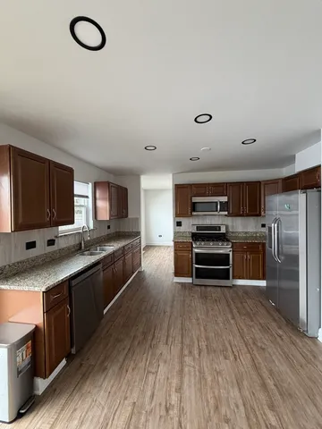 a large kitchen with stainless steel appliances a stove a sink dishwasher a refrigerator and a oven with wooden floor