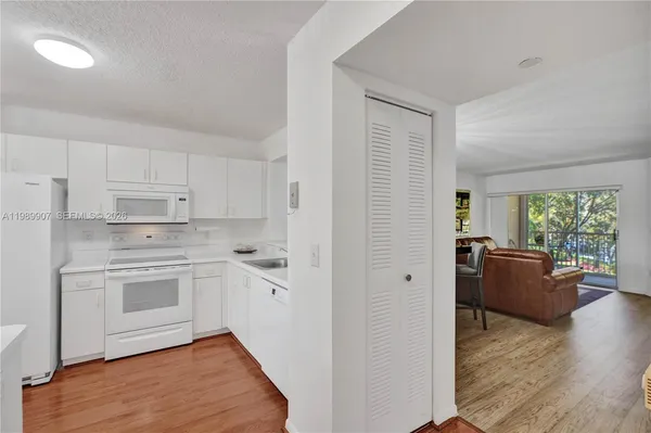 a kitchen with stainless steel appliances a stove a sink dishwasher a refrigerator white cabinets wooden floor and a dining table