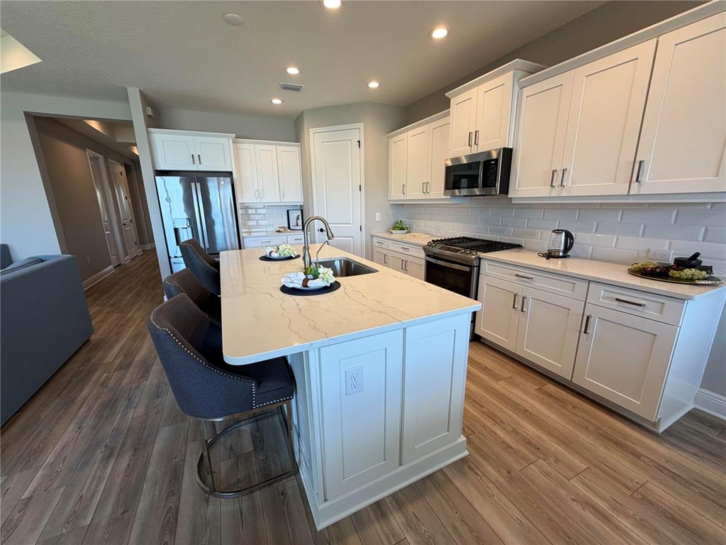 10710 Falling Leaf Court Parrish, FL 34219 - Photo 11 of 28 a kitchen with a sink a stove a microwave a refrigerator and white cabinets with wooden floor