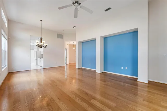 a view of an empty room with wooden floor and a ceiling fan