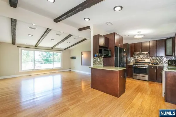 a large kitchen with stainless steel appliances kitchen island granite countertop a large refrigerator a stove and a wooden floors