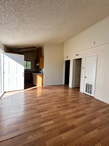 a view of an empty room with wooden floor and kitchen