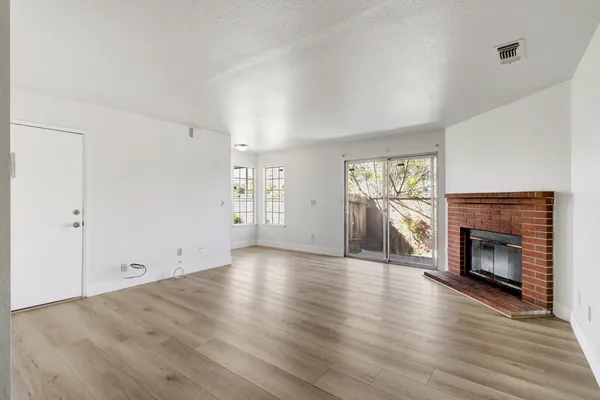 an empty room with wooden floor fireplace and windows