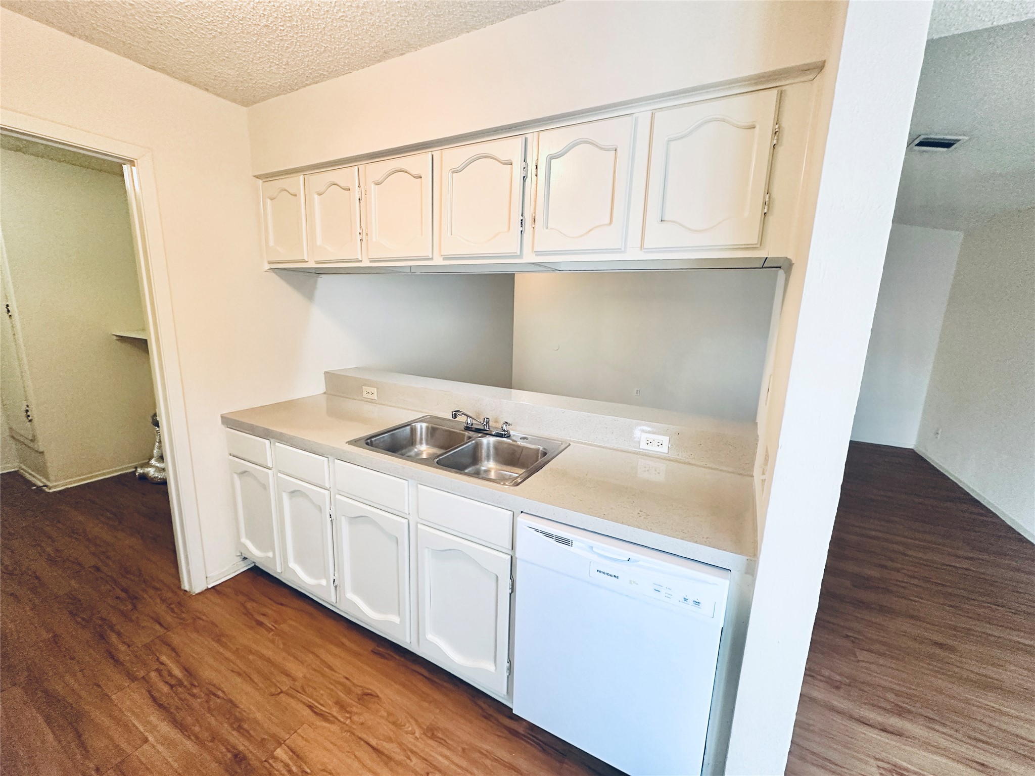 12504 Tree Line Drive, Unit B Austin, TX 78729 - Photo 8 of 22 Kitchen featuring a textured ceiling, white dishwasher, light countertops, dark wood-style flooring, and white cabinetry