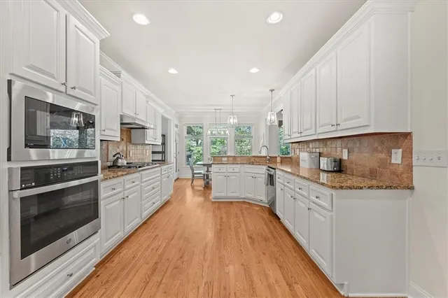 a kitchen with stainless steel appliances a stove top oven a sink a refrigerator white cabinets and wooden floor
