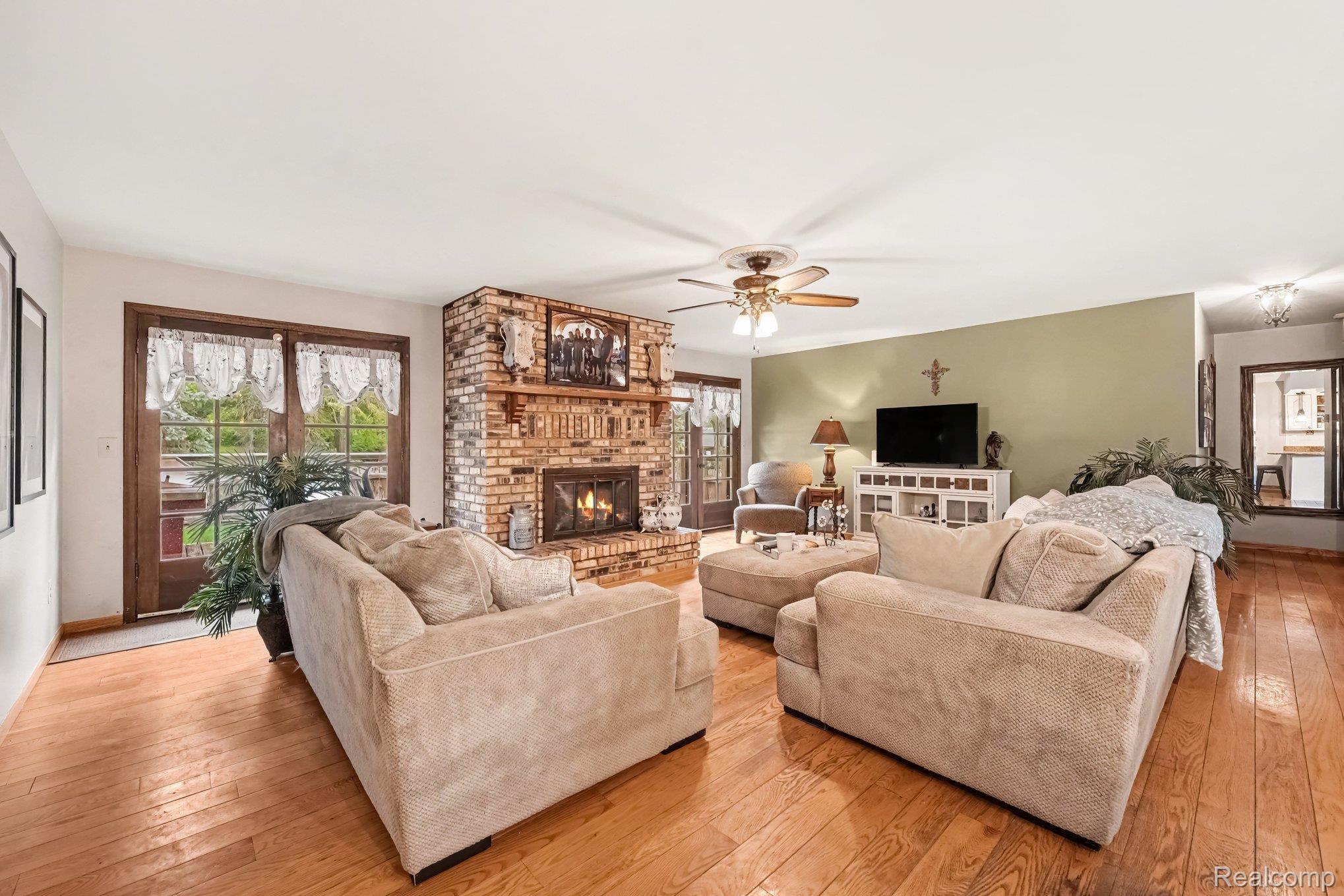107 Michelle Drive Romeo, MI 48065 - Photo 5 of 30 Hardwood flooring throughout, a brick fireplace, a ceiling fan, and double glass-paneled doors