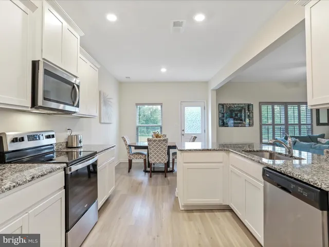 a kitchen with stainless steel appliances granite countertop wooden cabinets a sink dishwasher a stove and a refrigerator with wooden floor