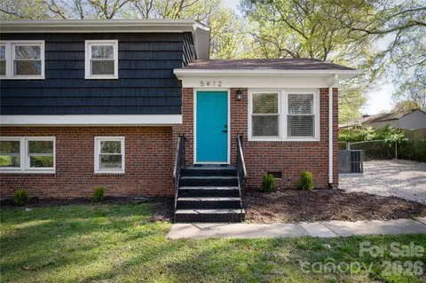 a view of a house with a small yard and a large tree