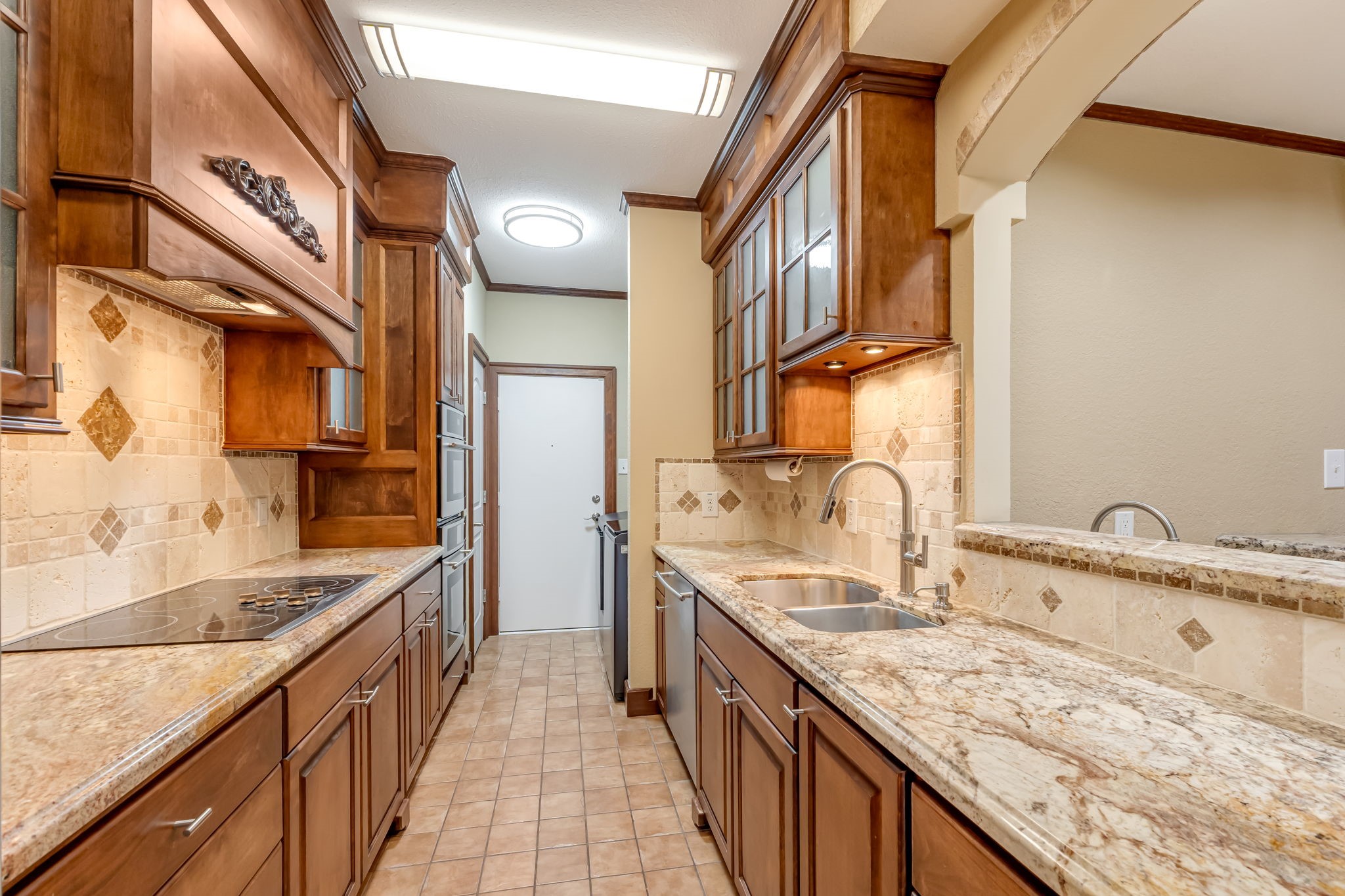516 South Post Oak Lane, Unit 18 Houston, TX 77056 - Photo 10 of 20 Well-eqipped kitchen with granite countertops, custom wood cabinetry, tile backsplash, and under-cabinet lighting. Features include electric cooktop, built-in oven and microwave, double-basin sink, and ample counter and storage space.
