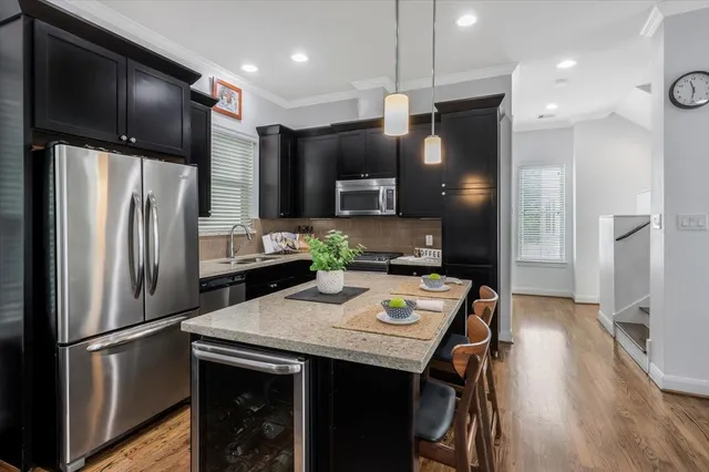 a kitchen with stainless steel appliances a refrigerator a sink a stove a kitchen island and chairs with wooden floor