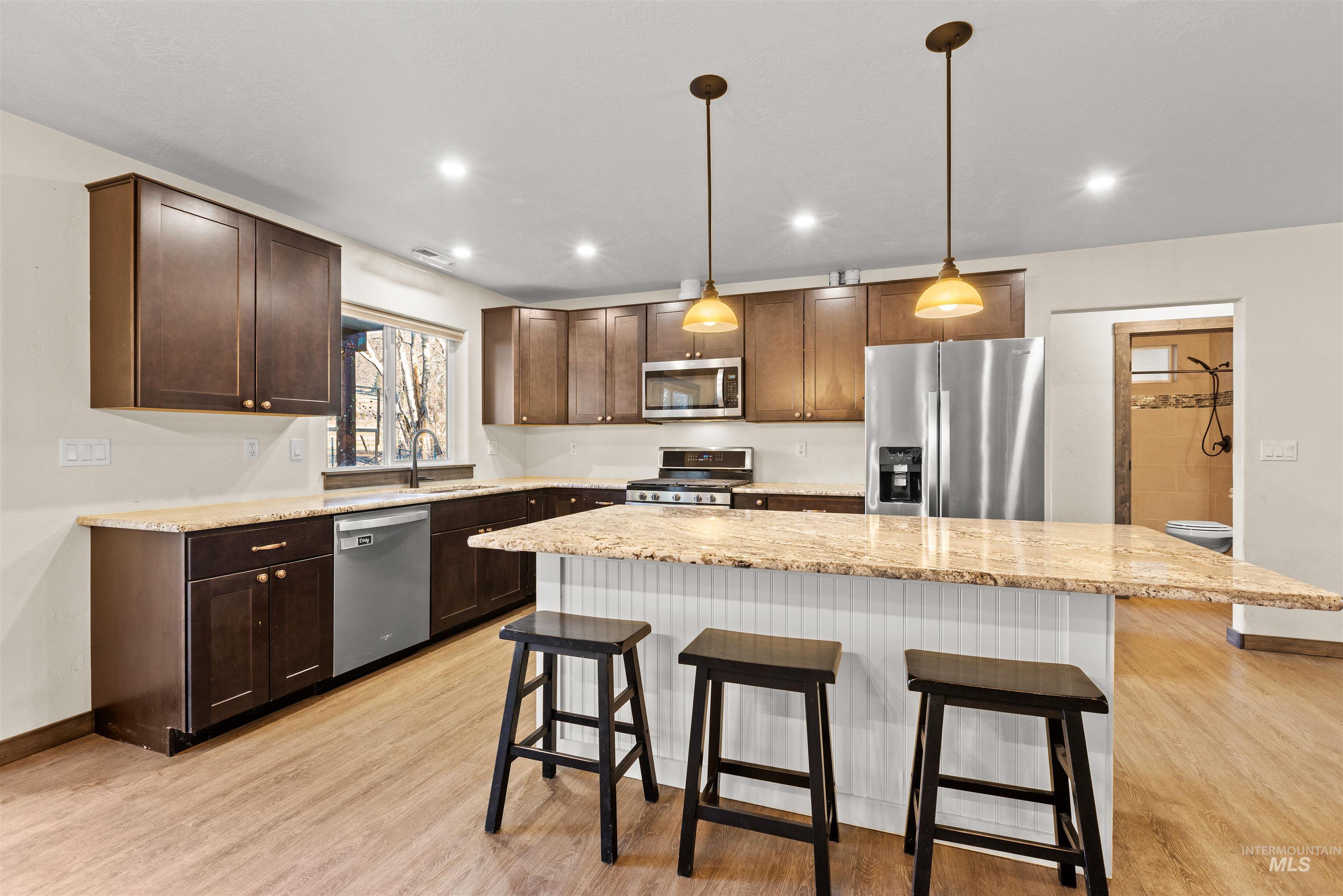 3488 Ward Road Cambridge, ID 83610 - Photo 18 of 50 Kitchen with a breakfast bar area, appliances with stainless steel finishes, pendant lighting, light stone countertops, and a center island
