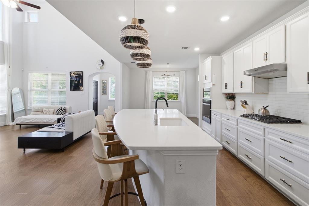 7416 Sequoia Rdg Road Little Elm, TX 76227 - Photo 22 of 37 Open-concept kitchen and living area featuring a large center island with integrated sink, white cabinetry with dark hardware, stainless steel appliances, and wood-finish flooring