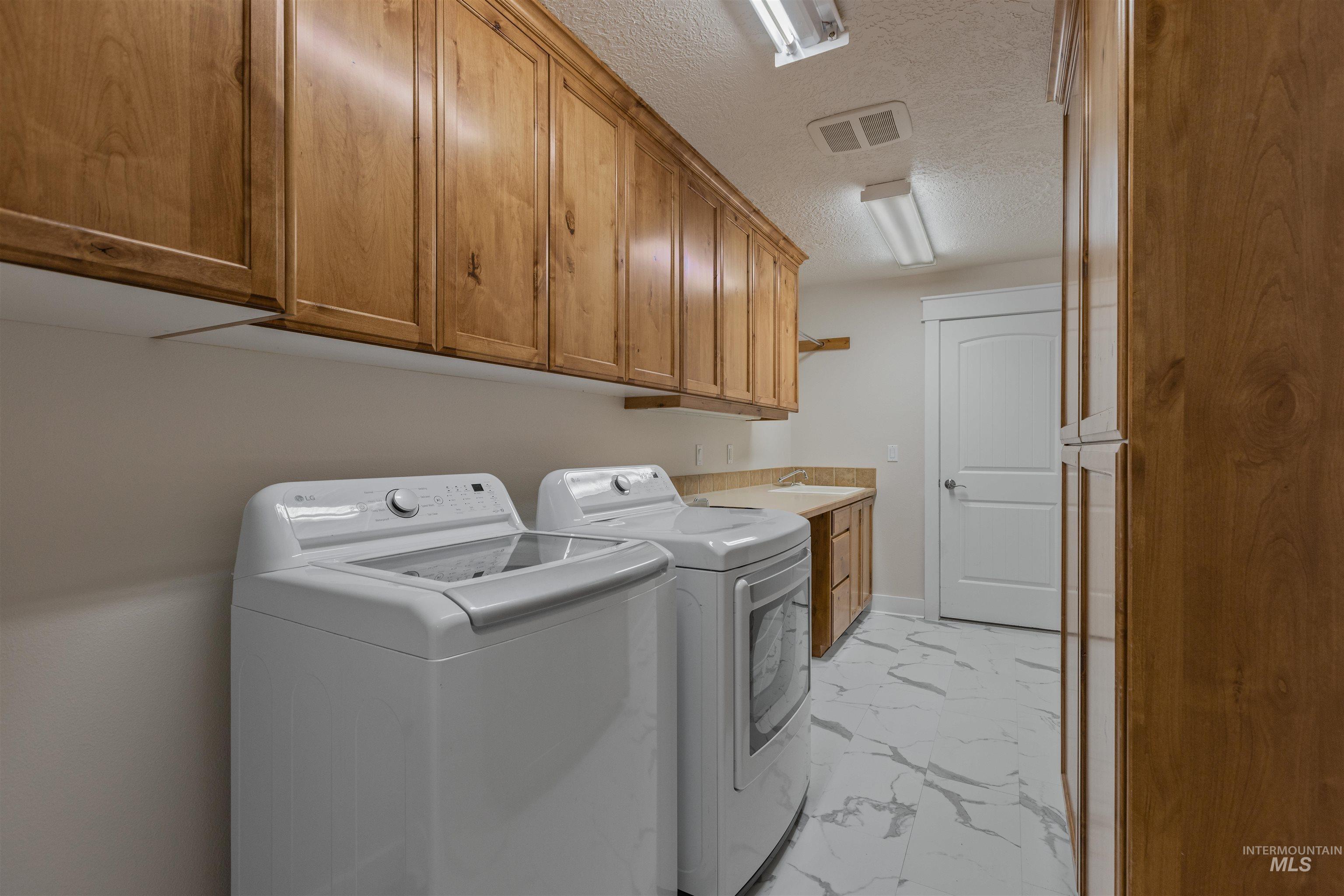 5426 West School Ridge Road Boise, ID 83714 - Photo 27 of 39 Laundry area featuring wood-finish cabinetry, a utility sink with a countertop, white door, and patterned floor tile