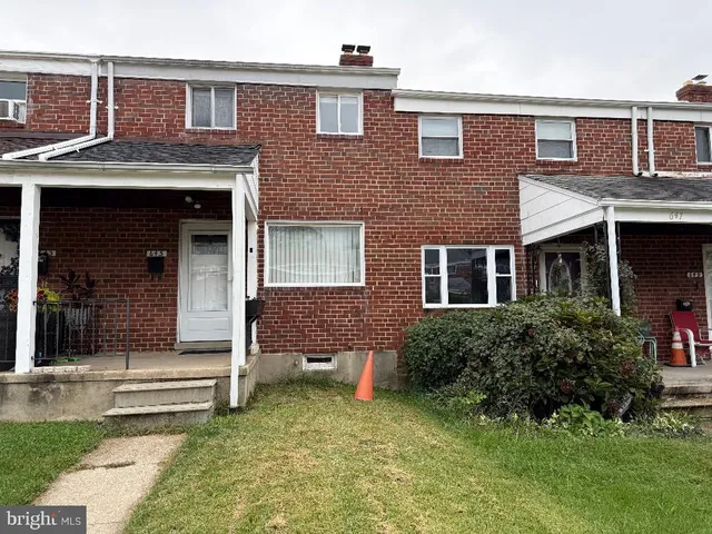 a view of a brick house with a yard plants and large tree
