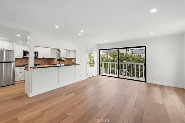 a view of a kitchen with stainless steel appliances granite countertop a stove a refrigerator a sink and a large window with wooden floor
