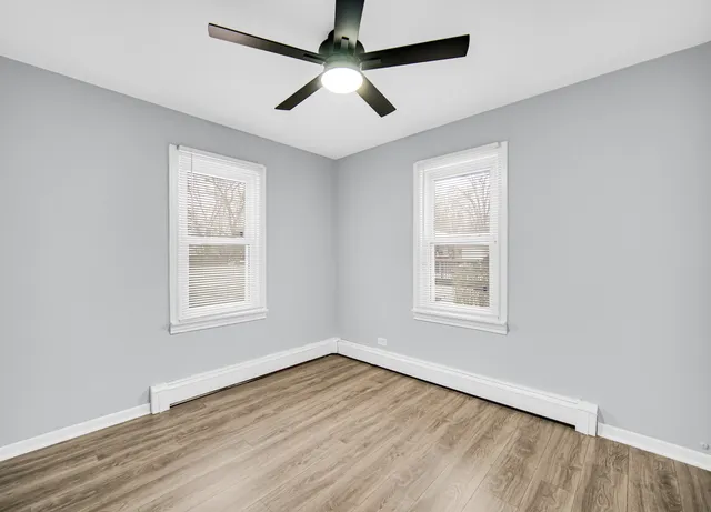 an empty room with wooden floor ceiling fan and windows