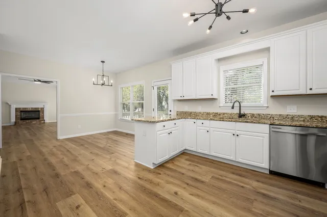a kitchen with granite countertop a stove a sink and white cabinets with wooden floor