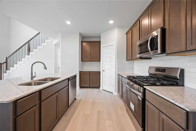 a kitchen with stainless steel appliances granite countertop a sink a stove top oven a refrigerator with wooden floors and cabinets