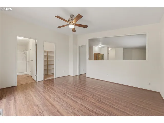 a view of an empty room with wooden floor and a ceiling fan