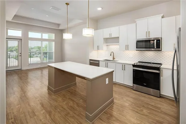 a kitchen with stainless steel appliances granite countertop a stove top oven a sink dishwasher and a refrigerator with wooden floor