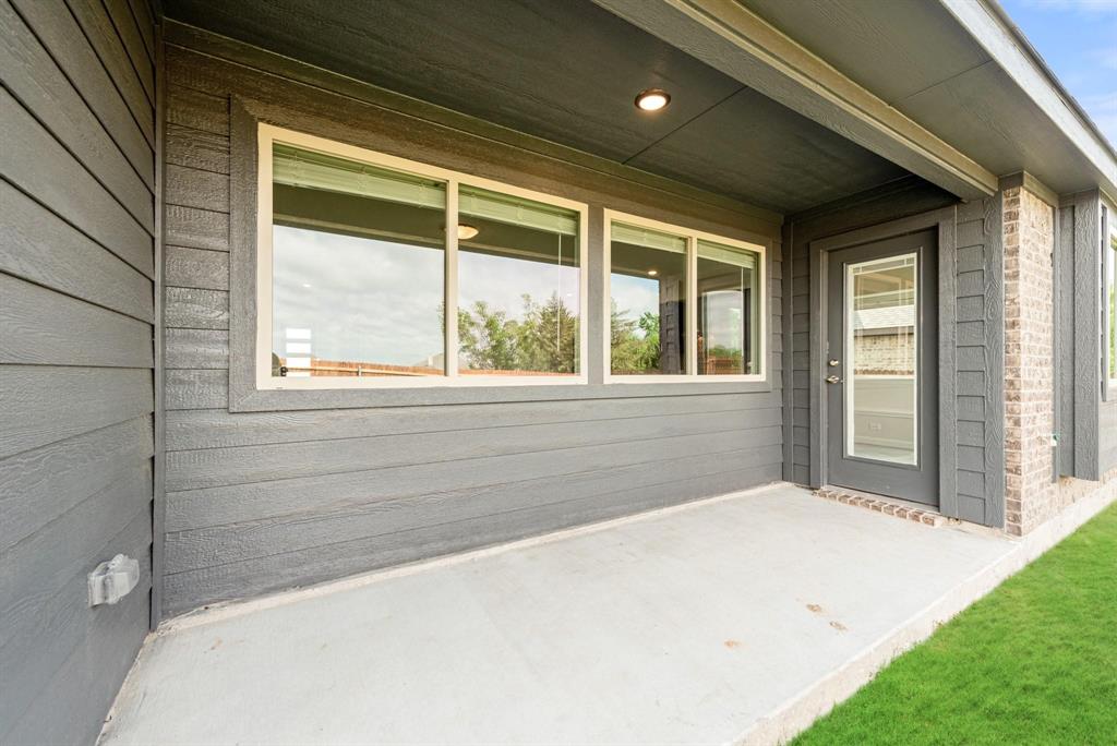 920 Elk Ridge Run Godley, TX 76044 - Photo 33 of 34 Covered patio with a concrete slab, showcasing a dark gray paneled exterior, brick accents, and a glass-paneled door