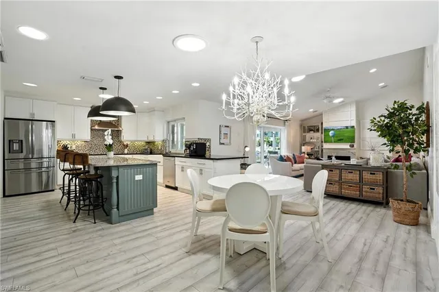 a kitchen with stainless steel appliances kitchen island granite countertop a refrigerator a stove a dining table and chairs with wooden floor