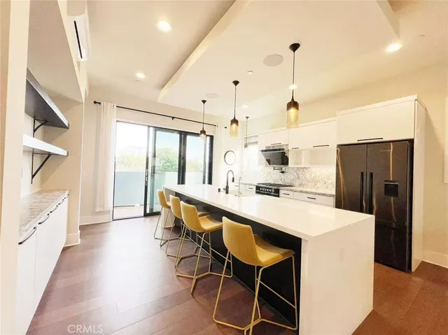 a kitchen with stainless steel appliances a stove a sink a refrigerator and white cabinets with wooden floor