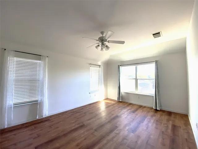 an empty room with wooden floor chandelier fan and windows