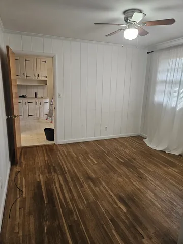 an empty room with wooden floor fan and windows