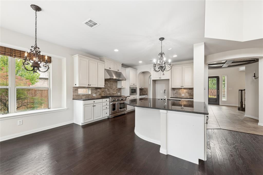 12571 Valley Spring Drive Frisco, TX 75035 - Photo 7 of 39 a kitchen with stainless steel appliances kitchen island granite countertop a stove a sink dishwasher a refrigerator and white cabinets with wooden floor