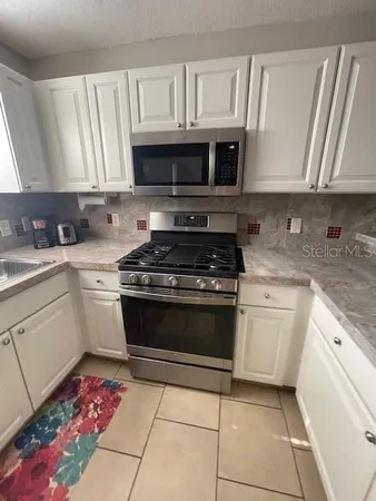 a white kitchen with granite countertop a stove top oven microwave and cabinets