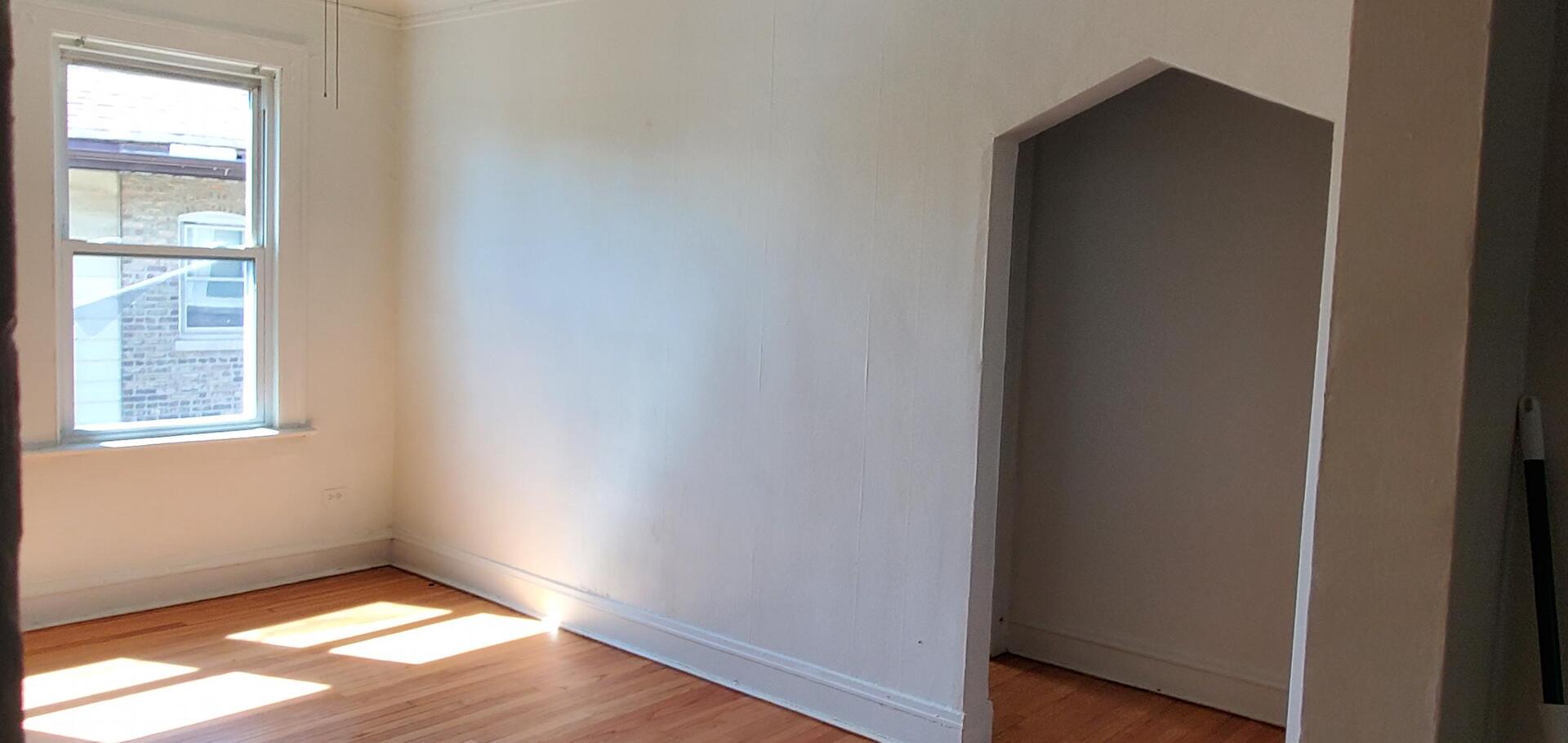 10801 South Indiana Avenue, Unit 2 Chicago, IL 60628 - Photo 4 of 10 a view of an empty room with wooden floor and a window