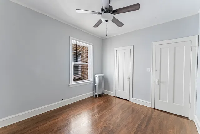 an empty room with wooden floor chandelier fan and windows