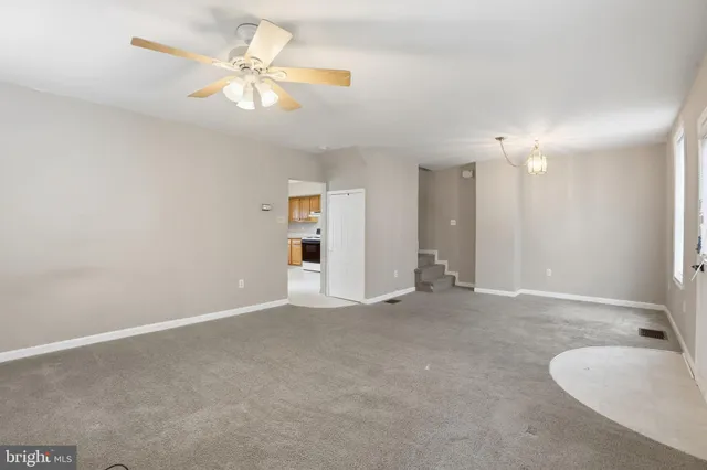 an empty room with chandelier fan and windows