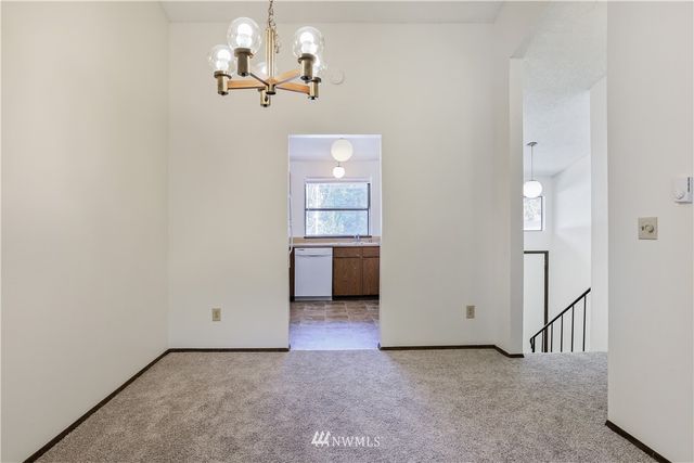 an empty room with a chandelier fan and kitchen view