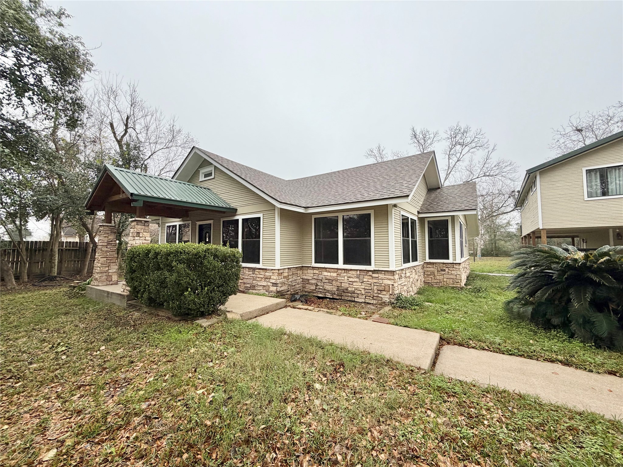 6219 Hamblen Drive Houston, TX 77396 - Photo 2 of 26 Charming single-story home with a blend of stone and siding exterior. Features a gabled roof, large windows, and a covered entryway with a metal roof. Surrounded by a spacious yard with mature trees and a paved walkway.
