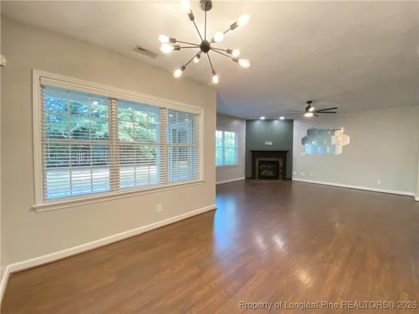 an empty room with wooden floor a chandelier fan and windows