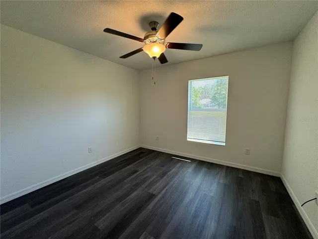 a view of an empty room with wooden floor and a ceiling fan