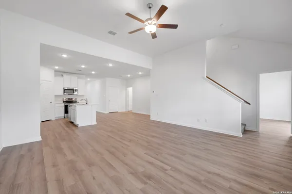 a view of an empty room with wooden floor and a ceiling fan