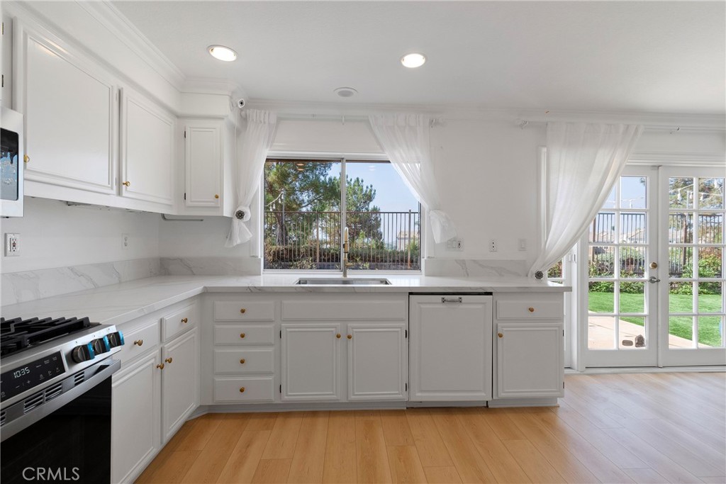 22 Carriage Drive Lake Forest, CA 92610 - Photo 7 of 35 a kitchen with stainless steel appliances granite countertop a stove a sink and white cabinets with wooden floor