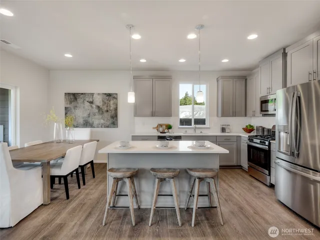 a kitchen with stainless steel appliances granite countertop a dining table chairs refrigerator sink and microwave