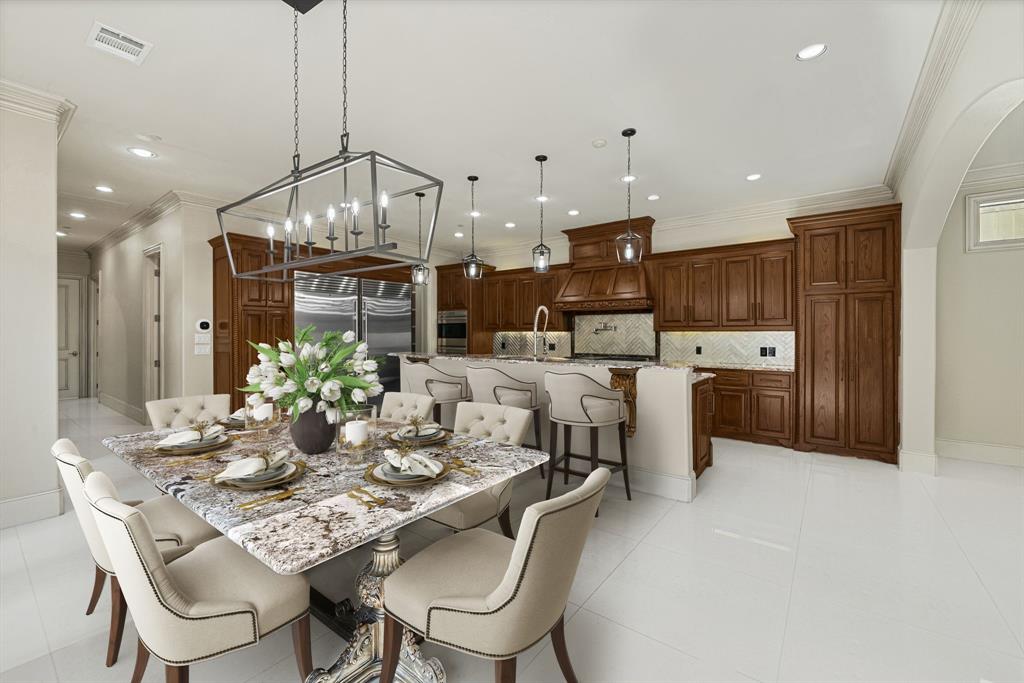 5821 Northaven Road Dallas, TX 75230 - Photo 8 of 40 Spacious open-concept kitchen and dining area featuring wood cabinetry, stainless steel appliances, a center island with bar seating, and a large dining table under a statement chandelier