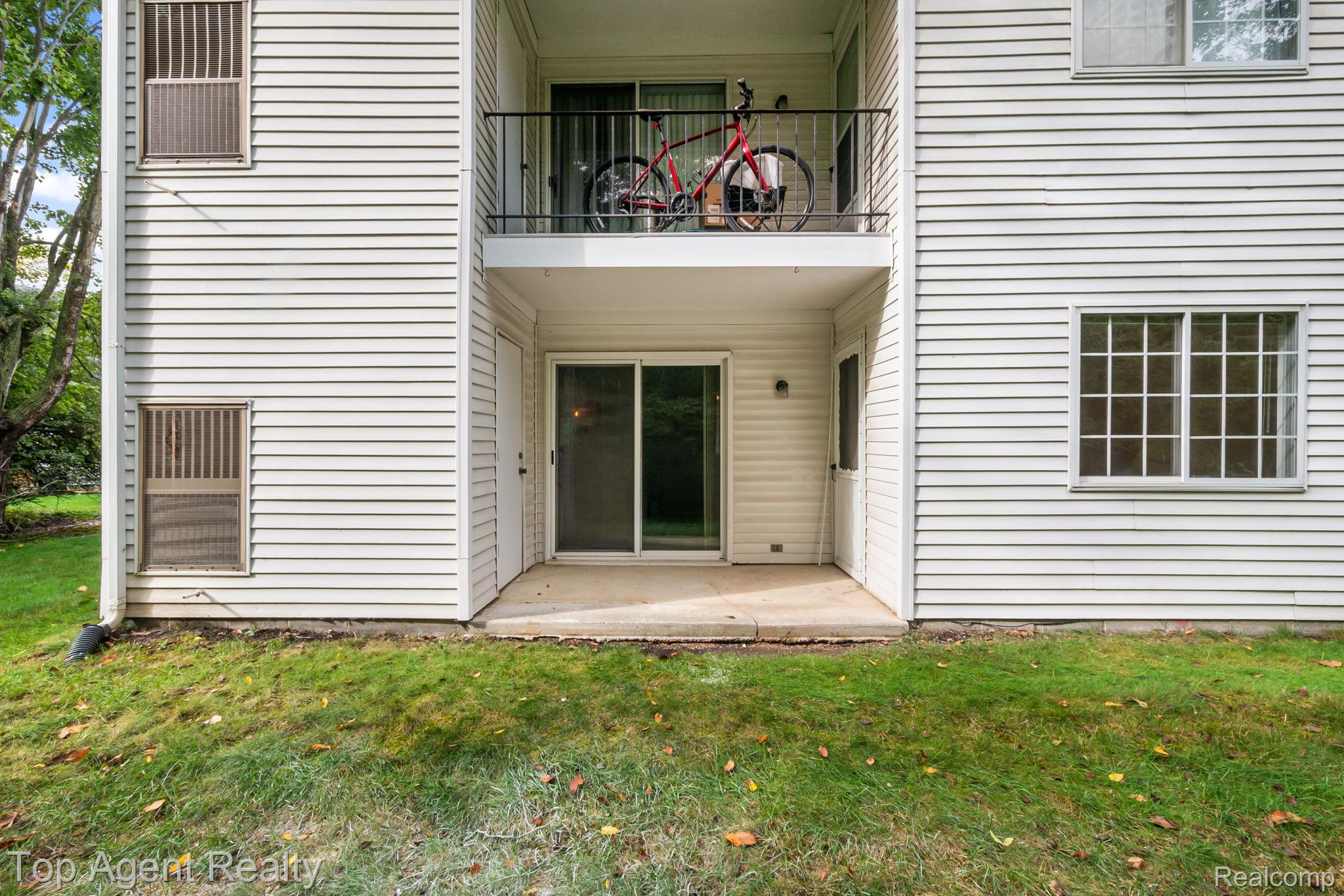 23420 Middlebelt Road Farmington, MI 48336 - Photo 26 of 32 White horizontal siding exterior with a ground-level patio, upper-level balcony with a black metal railing, and multiple windows