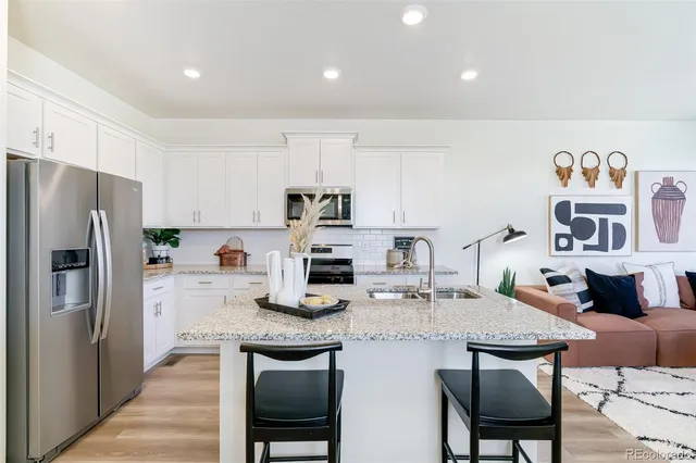 a kitchen with stainless steel appliances granite countertop a dining table chairs refrigerator and sink