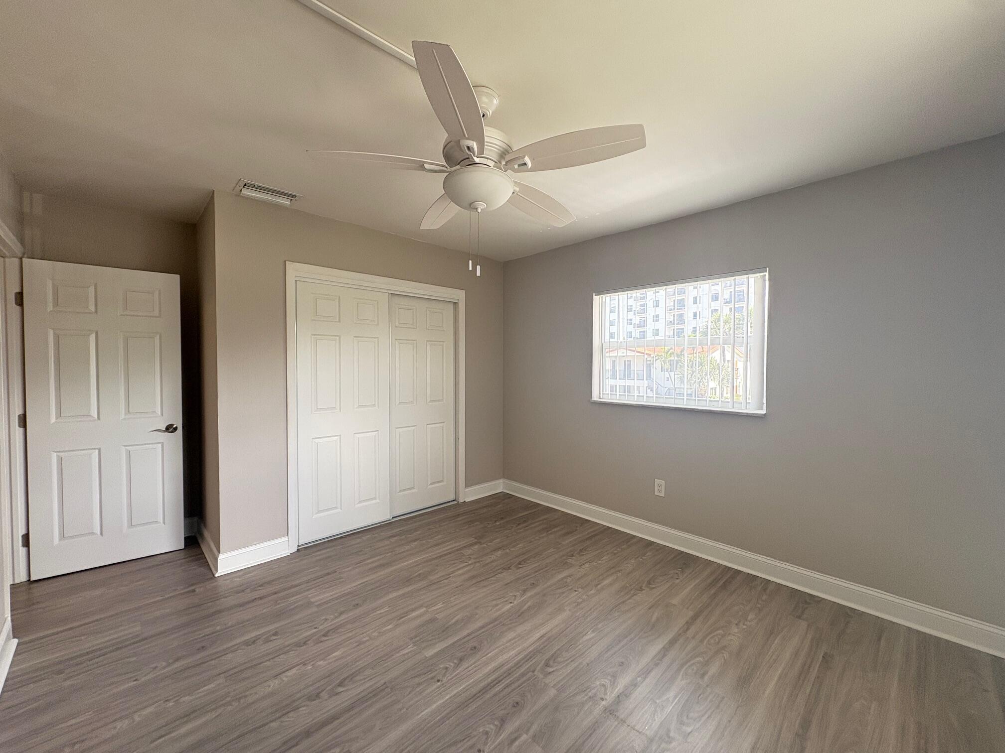 a view of an empty room with wooden floor and a ceiling fan