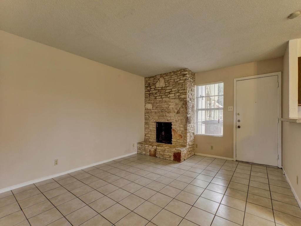 4300 Acropolis Court, Unit A Austin, TX 78759 - Photo 4 of 14 Unfurnished living room featuring a textured ceiling, light tile patterned floors, and a fireplace