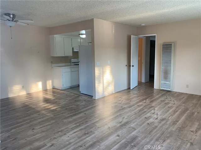 a view of empty room with wooden floor and kitchen