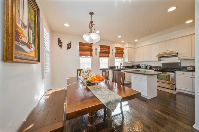 a kitchen with stainless steel appliances granite countertop a stove top oven a sink dishwasher a dining table and chairs with wooden floor